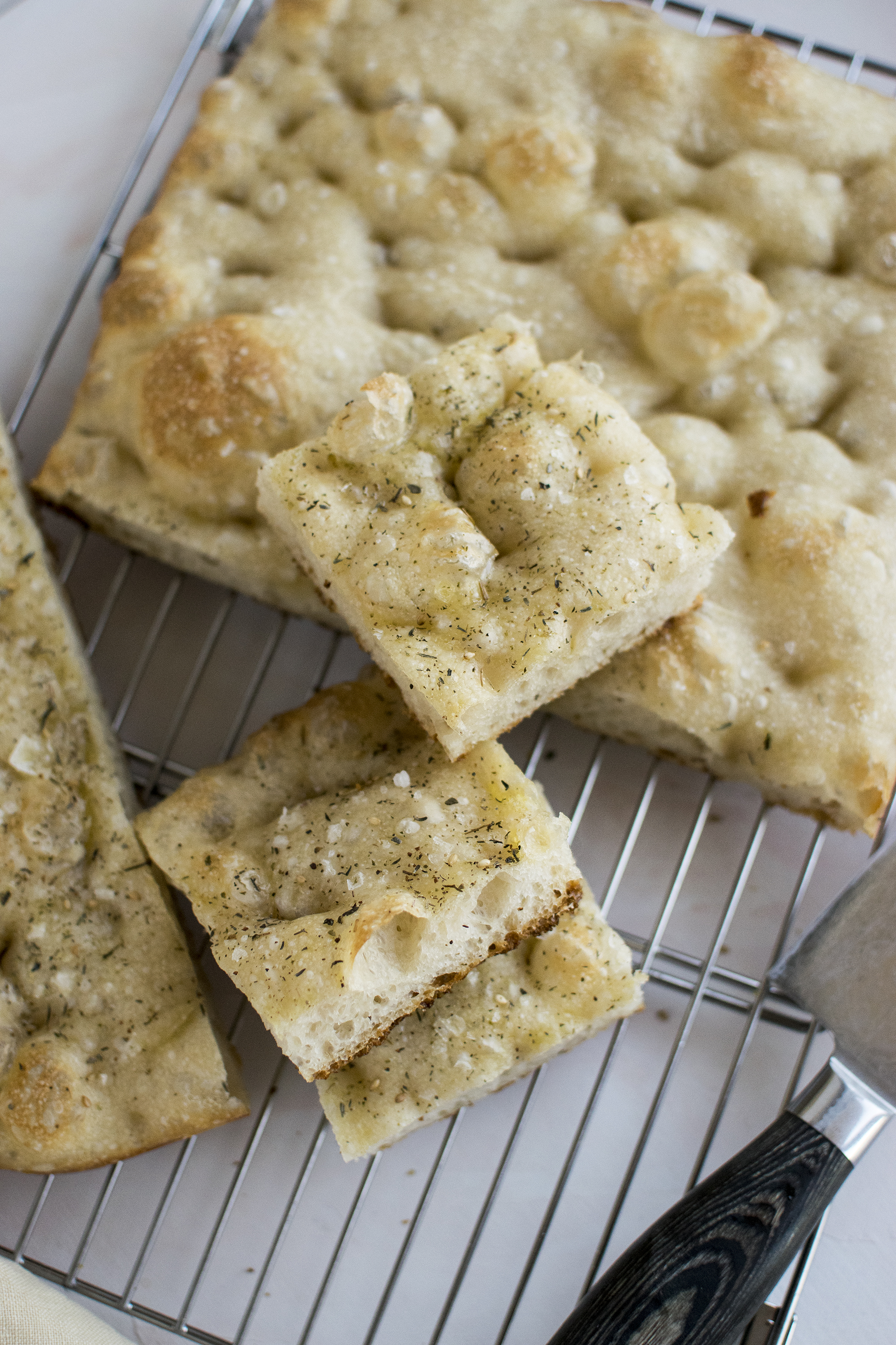 Focaccia with za'atar and salt flakes, cut in squares,  placed on a  cooling rack. 