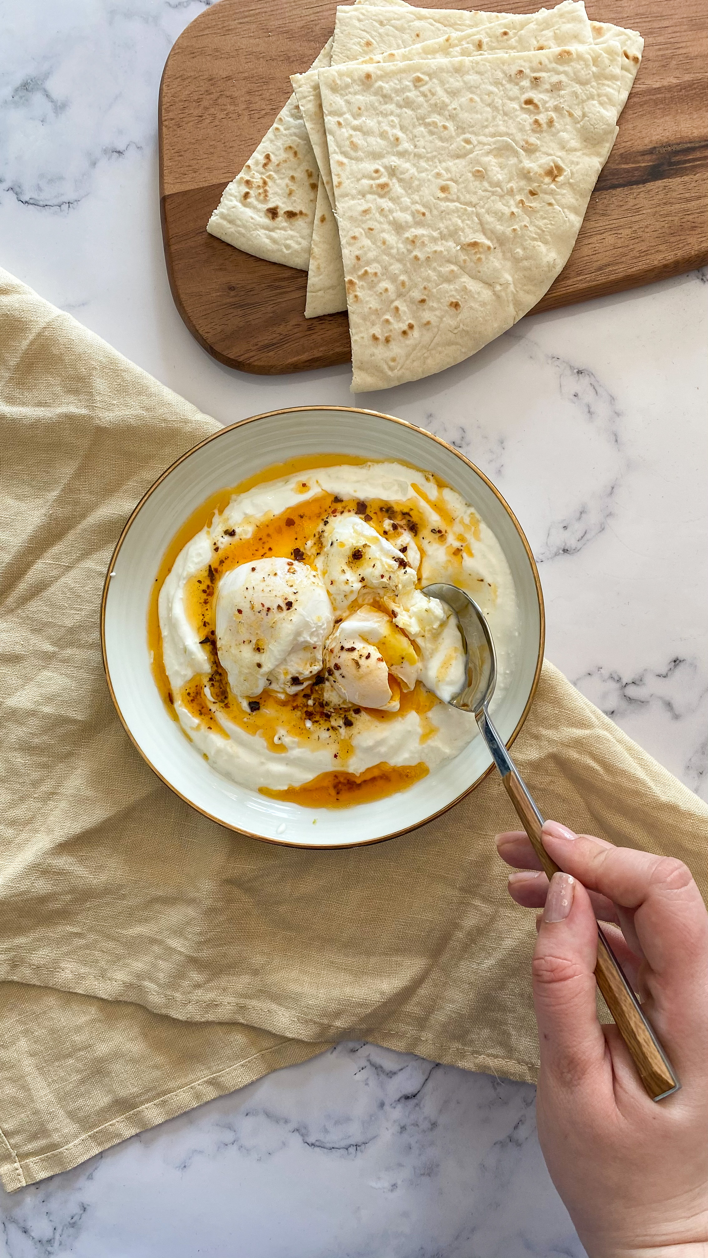 Small plate  with gold margin. Turkish eggs - bed of garlic yogurt, poached eggs, brown butter and chili flakes. 