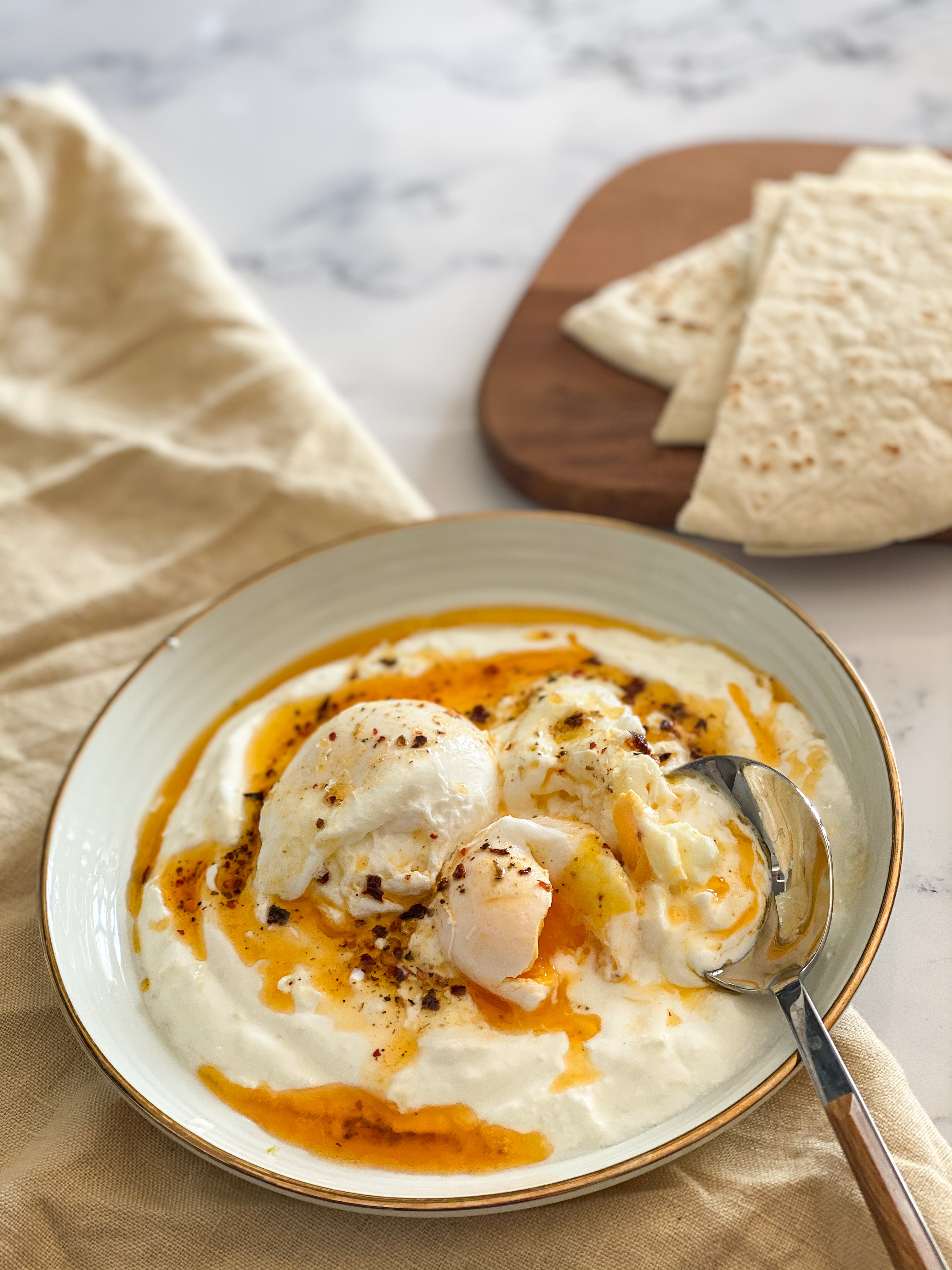 Small plate  with gold margin. Turkish eggs - bed of garlic yogurt, poached eggs, brown butter and chili flakes. 